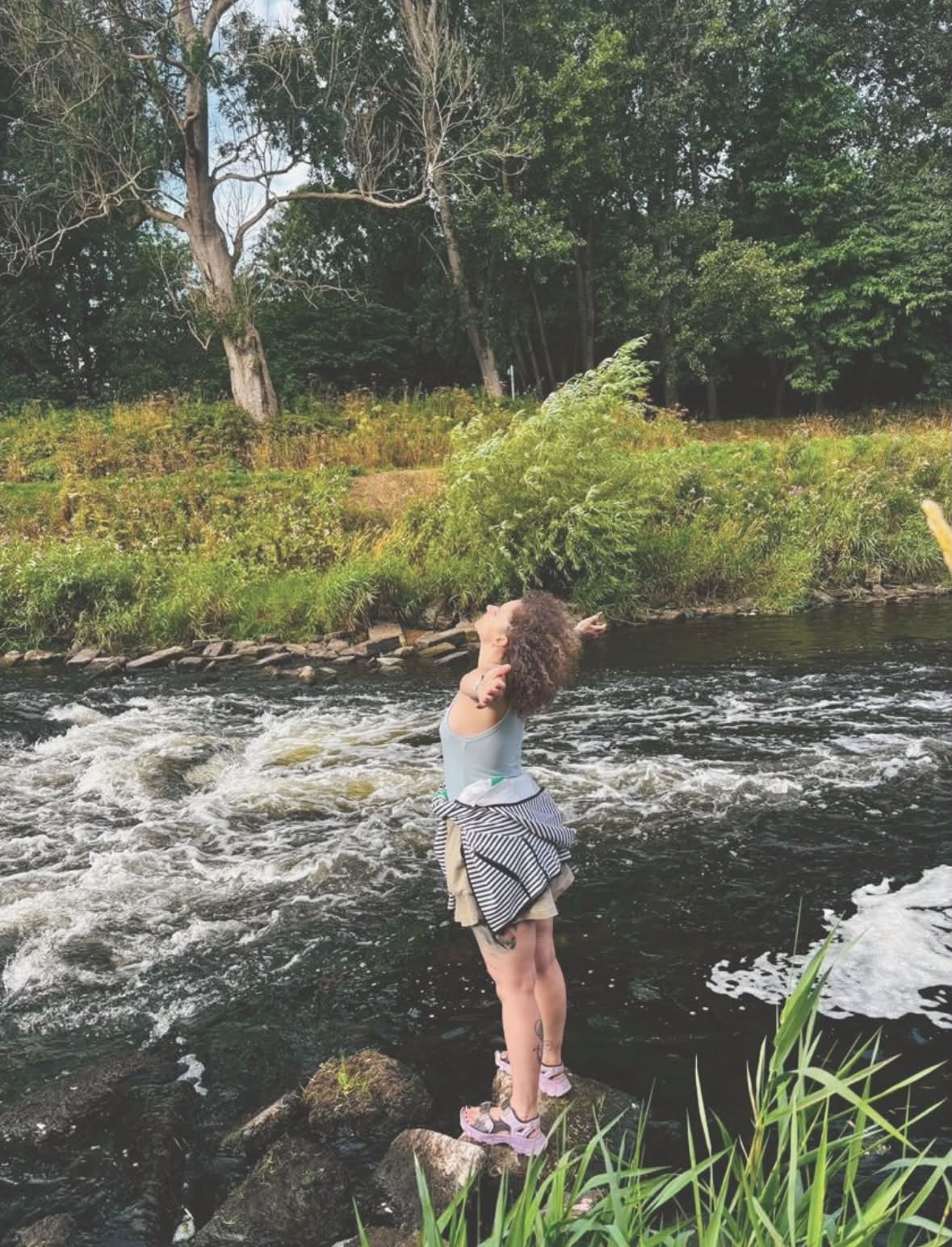 Paulina standing beside a river surrounded by greenery