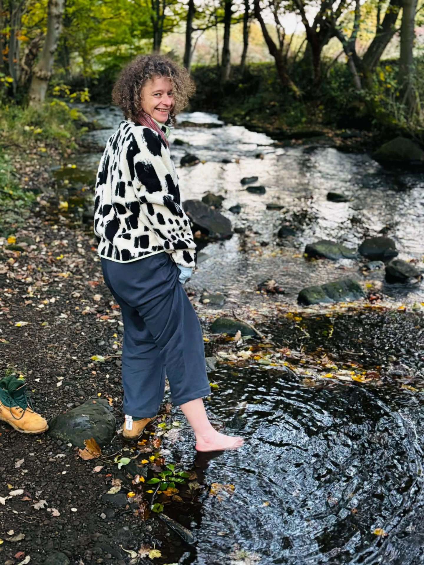 Paulina standing barefoot at the edge of a woodland stream in autumn