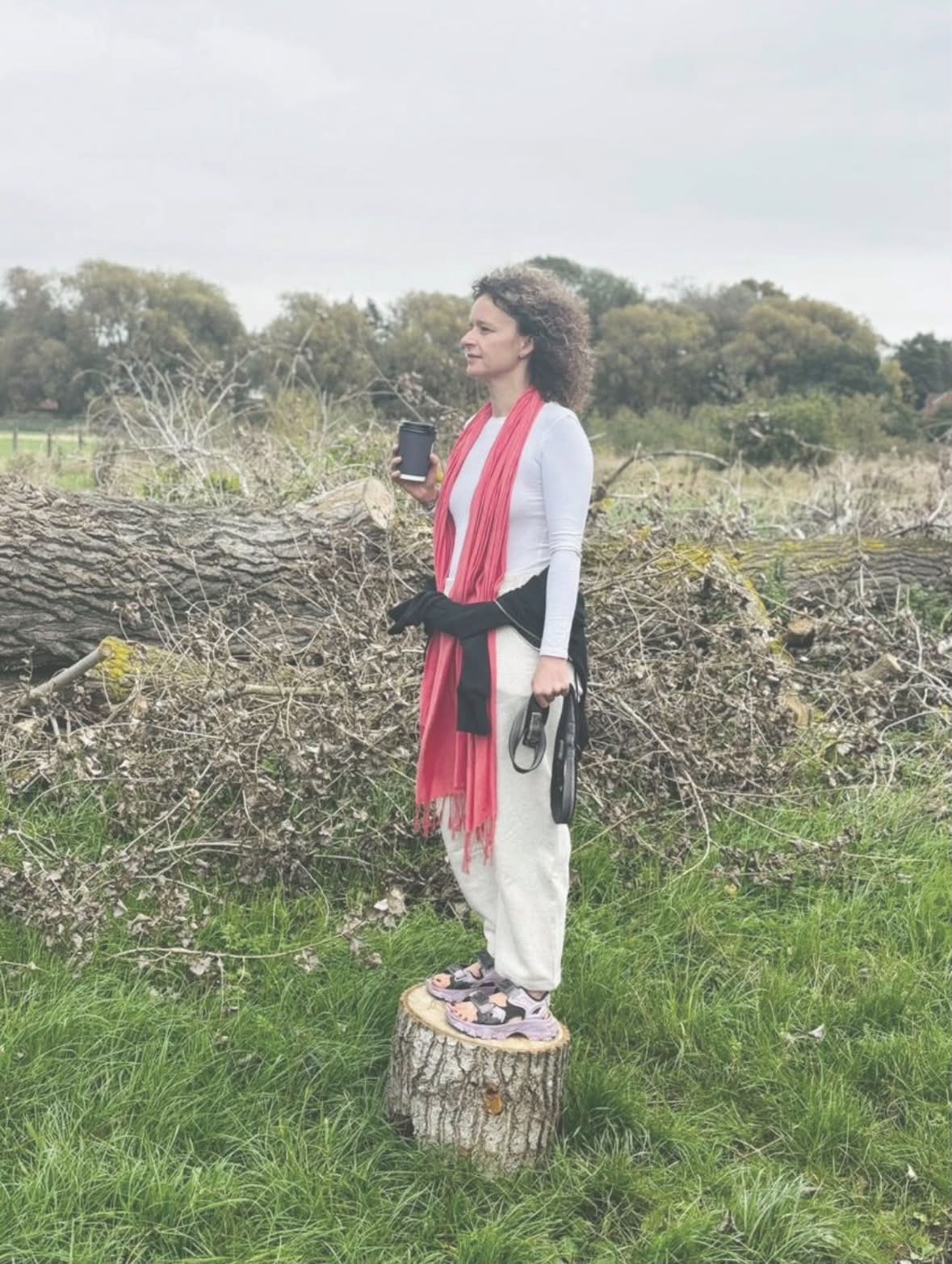 Paulina standing on a tree stump in an open field, holding a warm drink